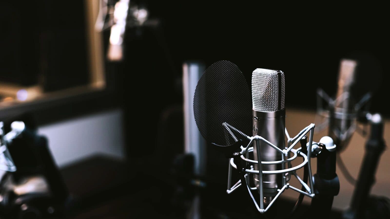 A studio condenser microphone on a boom arm in a dark booth.