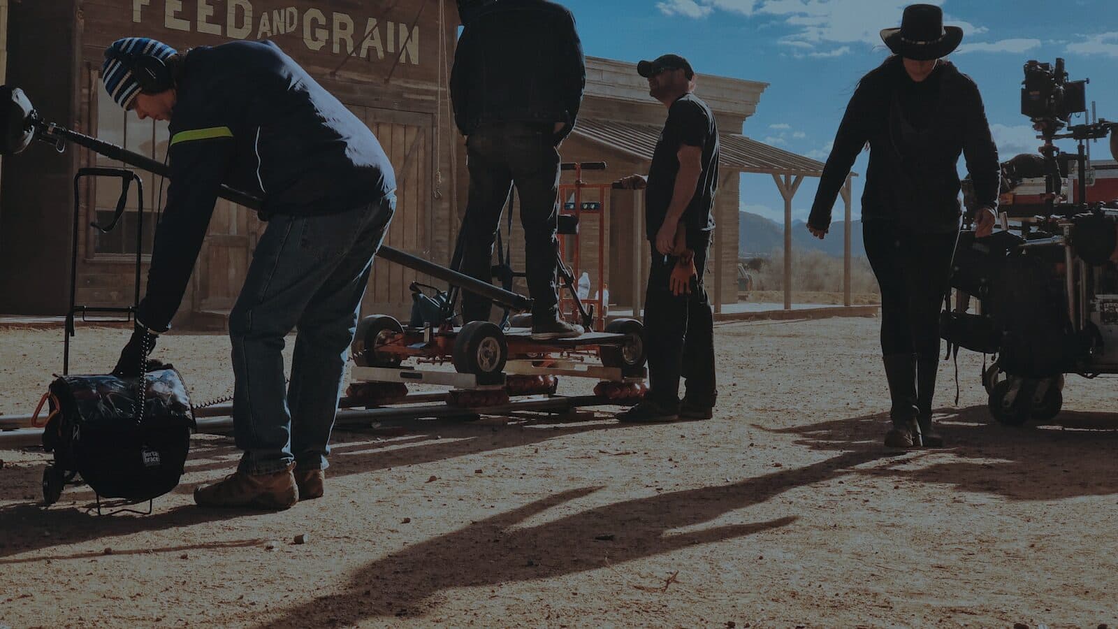 A crew on a location set, one of them laying dolly track while the camera stands ready behind them.
